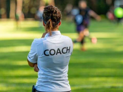 Frau von hinten mit T-Shirt auf dem "Coach" steht - Symbol für unsere Schreibtrainings