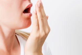 Eine Frau haucht, um zu prüfen, ob sie Mundgeruch hat - eventuell gähnt sie auch