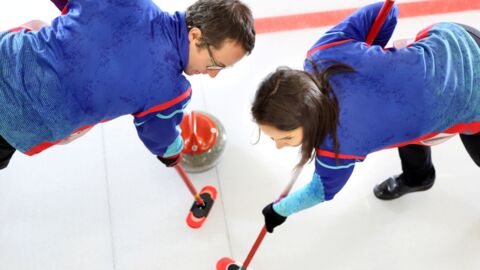 Zwei Curlingsportler wischen mit den Besen, damit der Curlingstein ins Zielfeld rutscht