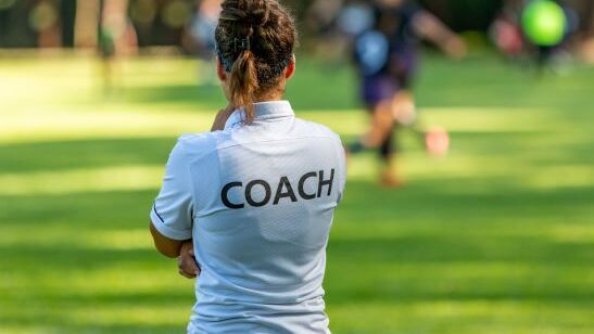 Frau von hinten mit T-Shirt auf dem "Coach" steht - Symbol für unsere Schreibtrainings