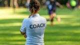 Frau von hinten mit T-Shirt auf dem "Coach" steht - Symbol für unsere Schreibtrainings