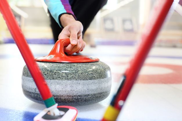 Auch schwere Inhalte können die Zielgruppe erreichen Ein Curlingstein und zwei Besen, die dafür sorgen, dass der Stein ins Zielfeld rutscht. Symbolbild für unsere Aussage: Wir bringen auch schwere Themen ins Ziel
