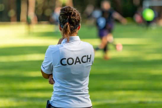 Frau von hinten mit T-Shirt auf dem "Coach" steht - Symbol für unsere Schreibtrainings